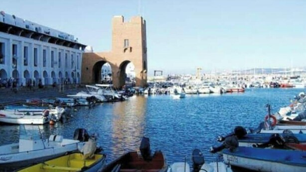 A marina with boats docked, a prominent tower, and a building with arches. - Great studio in El-Biar (Algiers)