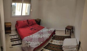 Cozy retreat with a single bed, bedside table, and nightstand, featuring a patterned rug and a window with a blind.