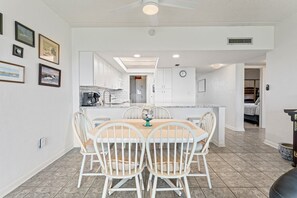 A modern kitchen with white cabinets, a dining area with a round table and four chairs, and a ceiling fan.