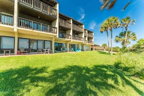 A multi-story hotel with balconies, outdoor seating, and a well-maintained lawn.