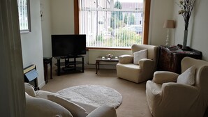 Una sala de estar con televisión, dos sillones, un sofá, una mesita y una lámpara.