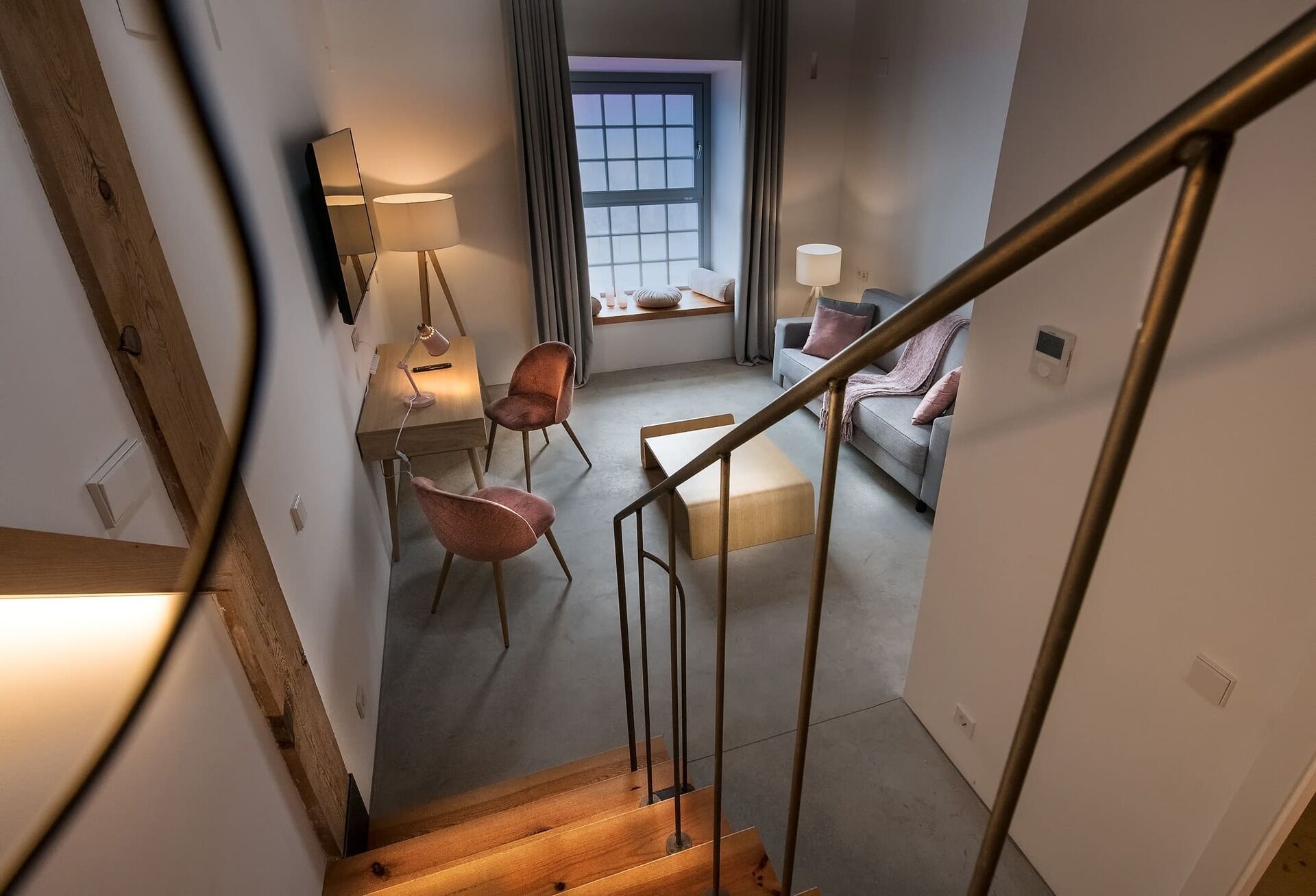 A staircase leading to a living area with a sofa, two chairs, a table, and a window with curtains.