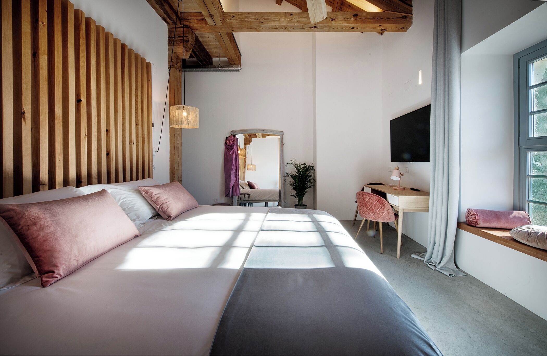 Ein Schlafzimmer mit einem großen Bett, einem Schreibtisch, einem Stuhl, einem Fernseher und einem Fenster.