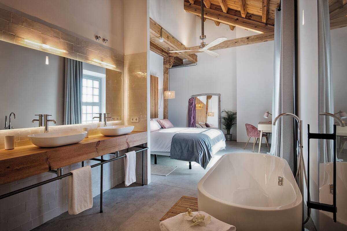 Un baño moderno con una bañera grande, dos lavamanos y una cama con vistas a la ciudad.