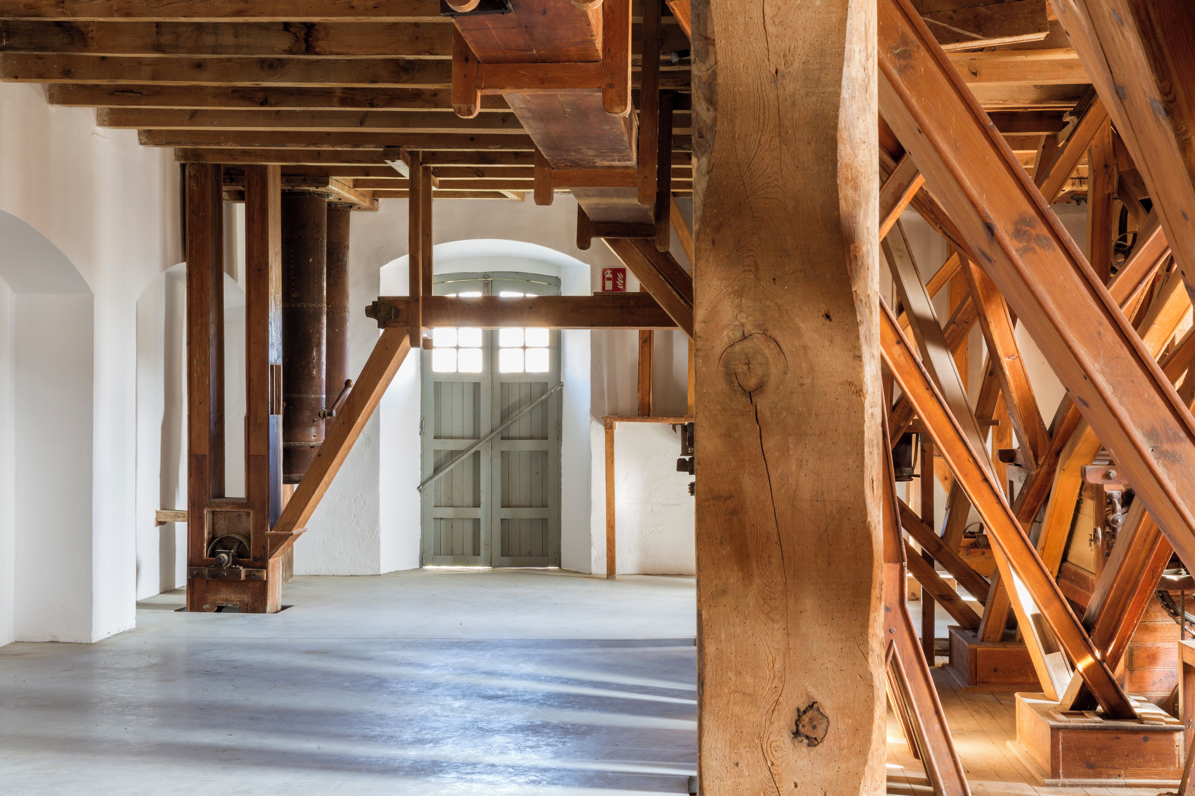 Una habitación espaciosa con techos altos y vigas de madera a la vista. Una amplia escalera de madera conduce a un nivel superior.