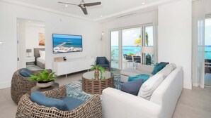 A modern living room with a sofa, wicker chairs, a coffee table, and a TV. - Rum Point Resort 201 by Grand Cayman Villas (Seven Mile Beach)