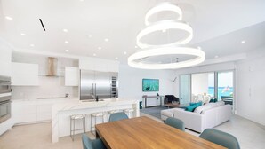 Cozinha moderna com ilha central, área de jantar com mesa de madeira e sala de estar com sofá e televisão.