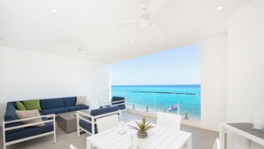 A modern living space with a white sofa, a dining table, and a view of the sea. - Rum Point Resort 405 by Grand Cayman Villas (Seven Mile Beach)