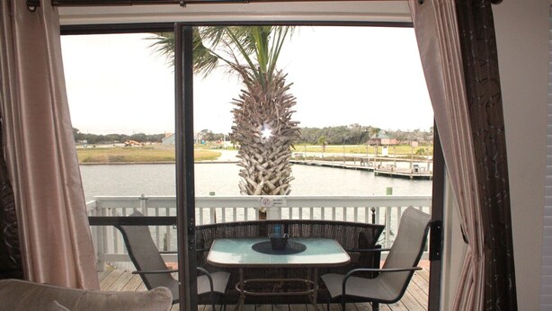 A balcony with a table and chairs, overlooking a body of water with a dock and a palm tree. - Bayfront canal side condo (Rockport)