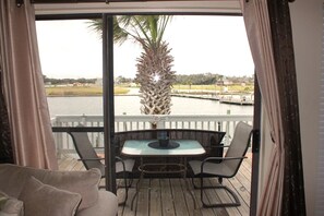 En balkon med et bord og stole, der kigger ud over et vandareal med en bro og en palme.