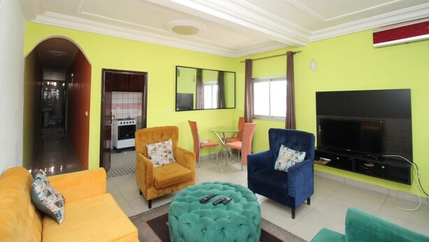 A living room with a sofa, armchairs, ottoman, TV, and a dining area with chairs. - Furnished apartment in Douala, Makepe (Douala)