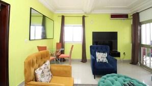 A living room with a yellow wall, a fireplace, a TV, and a sofa. - Furnished apartment in Douala, Makepe (Douala)