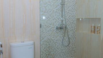 A bathroom with a toilet, a shower with a glass door, and a tiled wall.