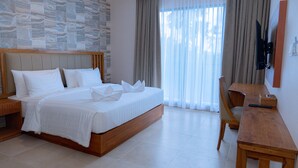 Ein Hotelzimmer mit einem großen Bett, einem Nachttisch aus Holz, einem Holzbüro, einem an der Wand montierten Fernseher und einer Wand mit Steinmusterung.