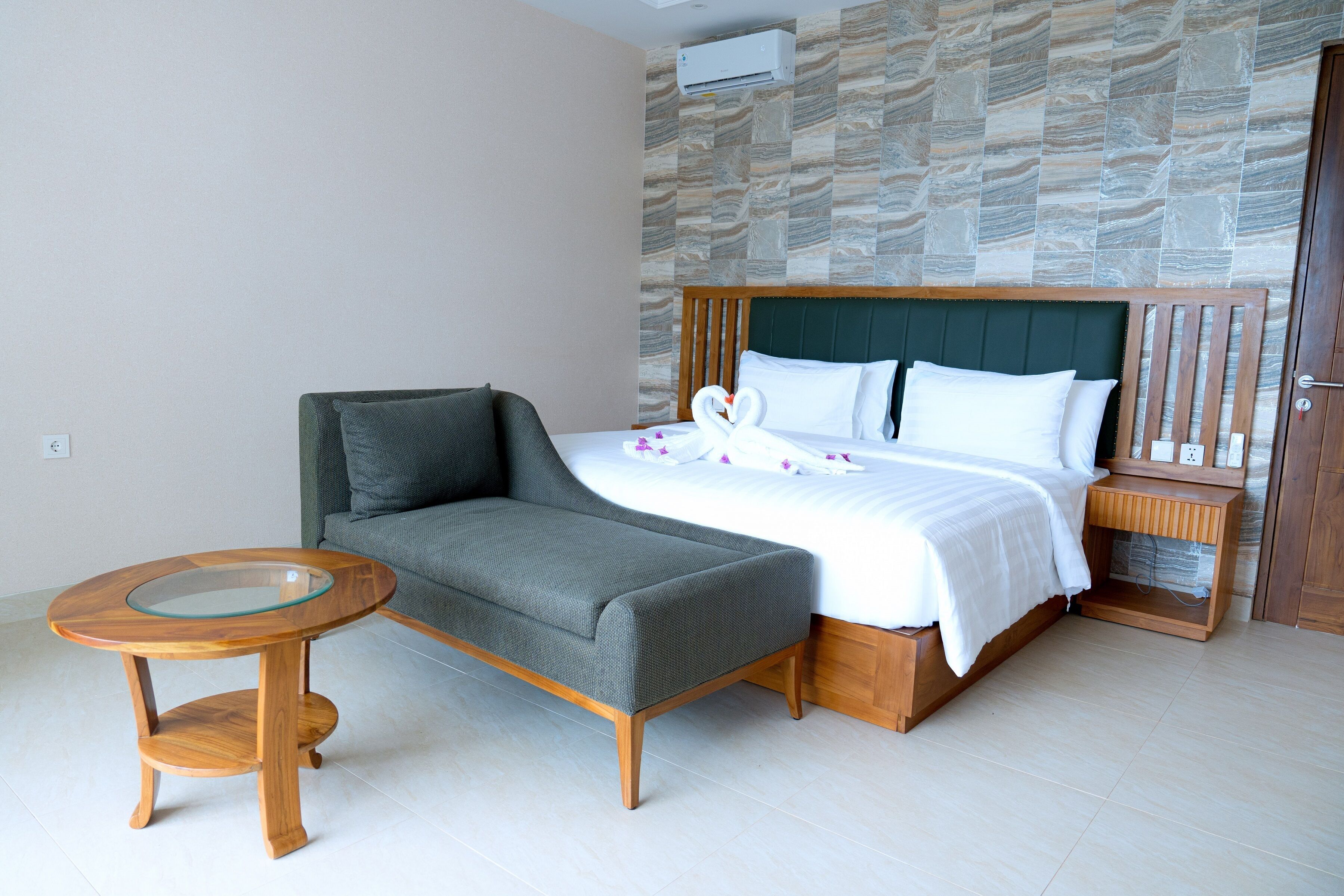 Une chambre à coucher comprenant un lit, un canapé, une petite table ronde et une table de chevet en bois.