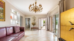 A spacious living room with a red leather sofa, a chandelier, a wooden cabinet, and a large window. - 3220 Villa Smeralda by Barbarhouse (Guagnano)