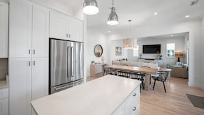 Una cocina moderna con armarios blancos, electrodomésticos de acero inoxidable, iluminación colgante y un comedor con una isla grande.