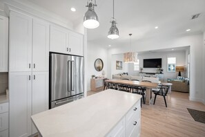 A modern kitchen with white cabinetry, stainless steel appliances, pendant lighting, and a dining area with a large island.