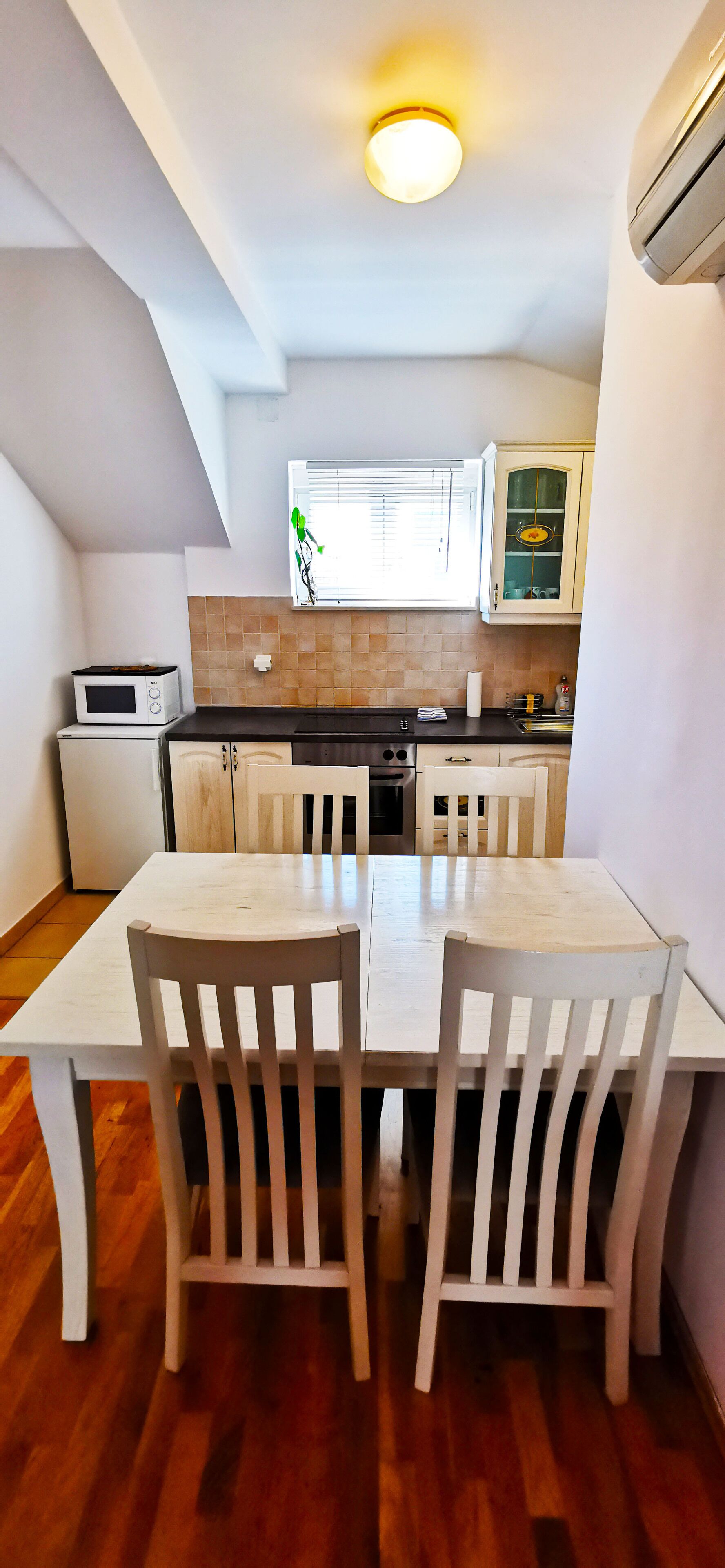 A compact kitchen with a dining table and chairs, a microwave, and a window with blinds.