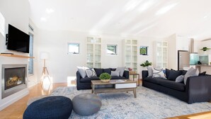 Een moderne woonkamer met een open haard, twee banken, een salontafel en ingebouwde kasten met glazen deuren.