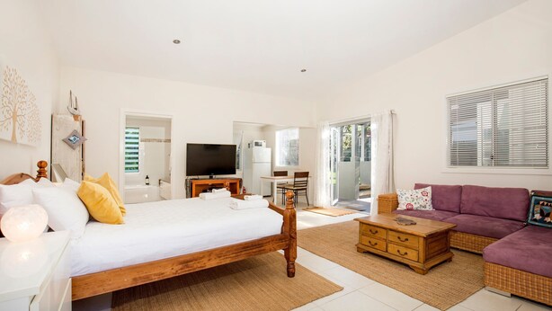 A spacious room with a large bed, a television, a dining area, and a sofa. - Hyams Drift + Studio (Hyams Beach)