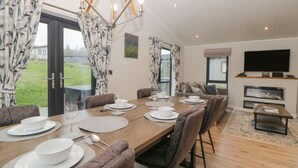 A dining area with a wooden table set for four, surrounded by chairs. There is a television and a fireplace in the background. - Meadow Lodge (Lifton)