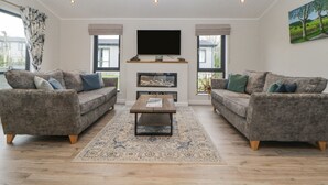 A living room with two grey sofas, a wooden coffee table, a flat-screen TV, and a fireplace. - Meadow Lodge (Lifton)