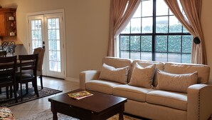 Una sala de estar con sofá, mesa de centro, sillón floral, mesa de comedor con sillas y una araña.