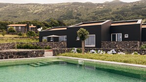 Un edificio moderno con piscina, pareti in pietra e vista su colline verdi.