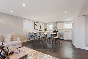 Una cocina moderna con armarios blancos, una zona de comedor con sillas grises y un sofá gris.