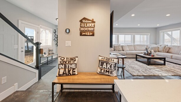 Een moderne woonkamer met een trap, een zithoek en decoratieve kussens met de tekst ‘Jump in the Lake’ en ‘Lake Time’.