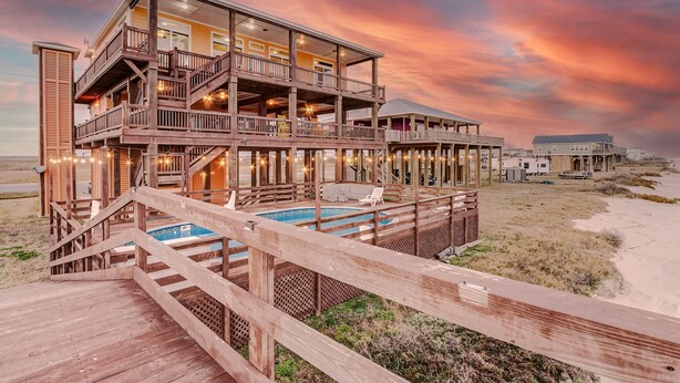 Un edificio de madera de varios pisos con piscina, terraza y vista a la playa.