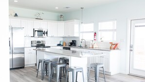 Una cocina moderna con armarios blancos, electrodomésticos de acero inoxidable y una isla central con taburetes de bar.