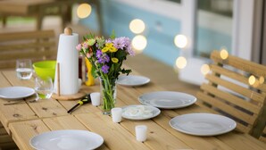Una mesa de madera preparada para comer, con platos blancos, un jarrón de flores y una vela.