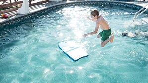 Una persona saltando a una piscina con una colchoneta flotante.