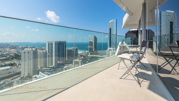 Un balcon situé dans un immeuble de grande hauteur, offrant une vue dégagée sur les toits de la ville et l’océan.
