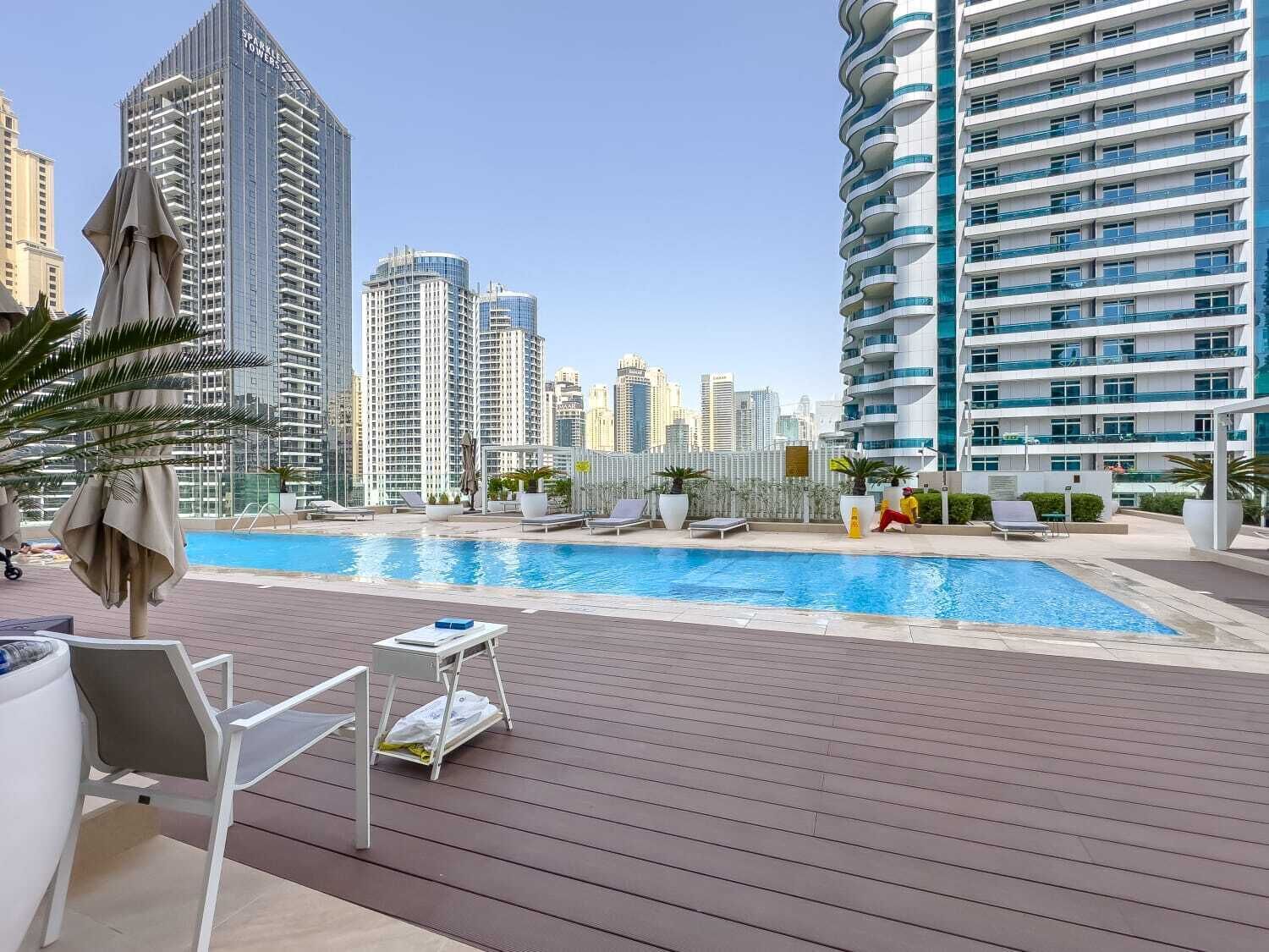 A rooftop pool area with lounge chairs and umbrellas, surrounded by high-rise buildings.