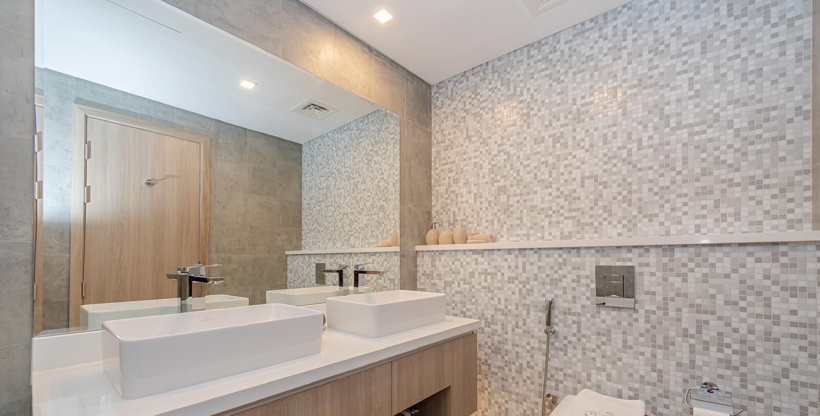 A modern bathroom with two large white sinks, a wooden door, and a tiled shower area.