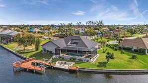 Ein modernes Haus mit einer großen Terrasse, einem Swimmingpool und einem Steg, der ins Wasser führt.