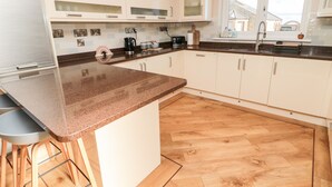 A modern kitchen with a granite countertop, wooden flooring, and white cabinetry. - The Croft (Alnwick)