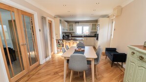 A modern kitchen with a dining area, wooden flooring, and a view of the outside. - The Croft (Alnwick)