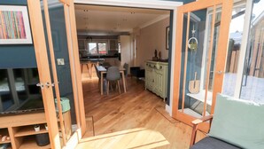 An open-plan living space with a dining area, kitchen, and a large window with a view. - The Croft (Alnwick)