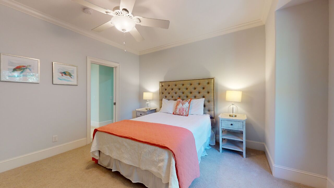 Une chambre à coucher comprenant un lit, deux tables de chevet, un ventilateur de plafond et des œuvres d’art encadrées accrochées au mur.