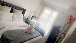 Ein ordentlich eingerichtetes Schlafzimmer mit Bett, Nachttisch und einem Fenster mit Vorhängen.