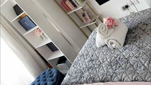 Ein Schlafzimmer mit einem Bett, einem an der Wand montierten Fernseher, einem Bücherregal und einem Fenster.