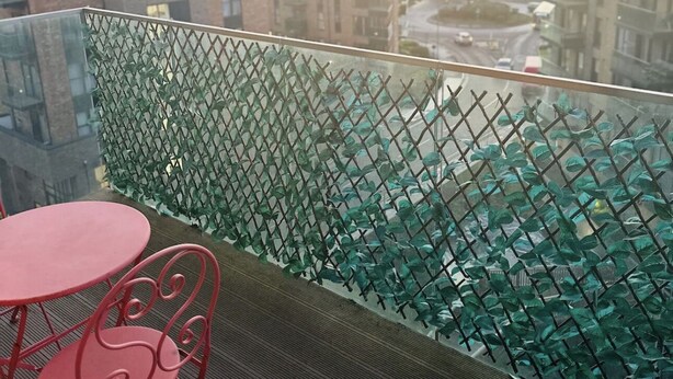 Ein Balkon mit Glasabschluss, einem roten Metallstuhl und einem Tisch.