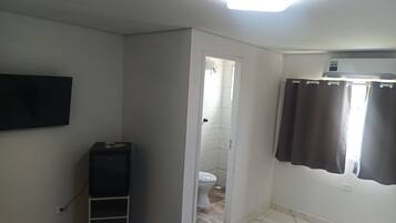 A hotel room with a bed, a flat-screen TV mounted on the wall, a small cabinet, a shower area, and a curtain.