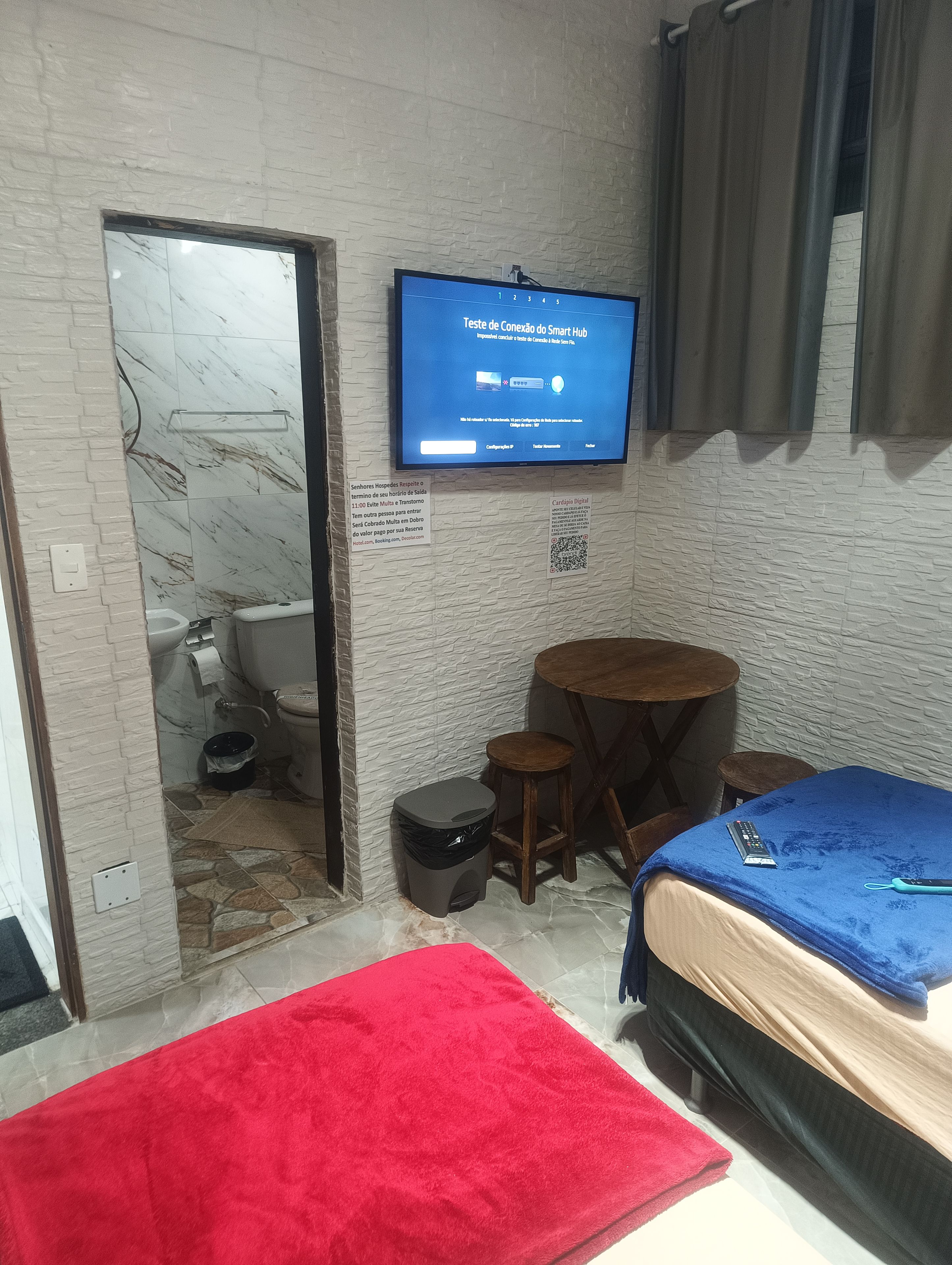 A compact room with a bed, a small table, a TV mounted on the wall, and a bathroom visible through an open door.