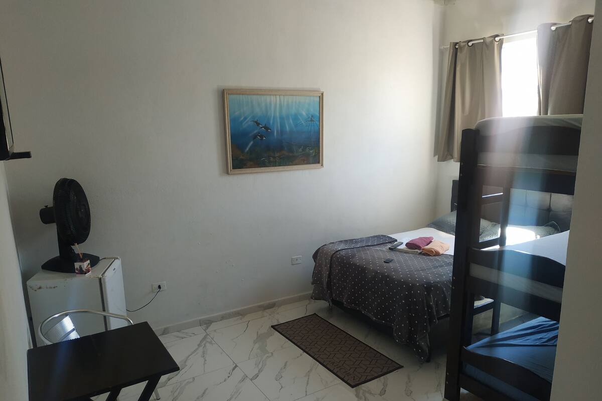 A bedroom with a bunk bed, a desk with a fan, a painting on the wall, and a window with curtains.