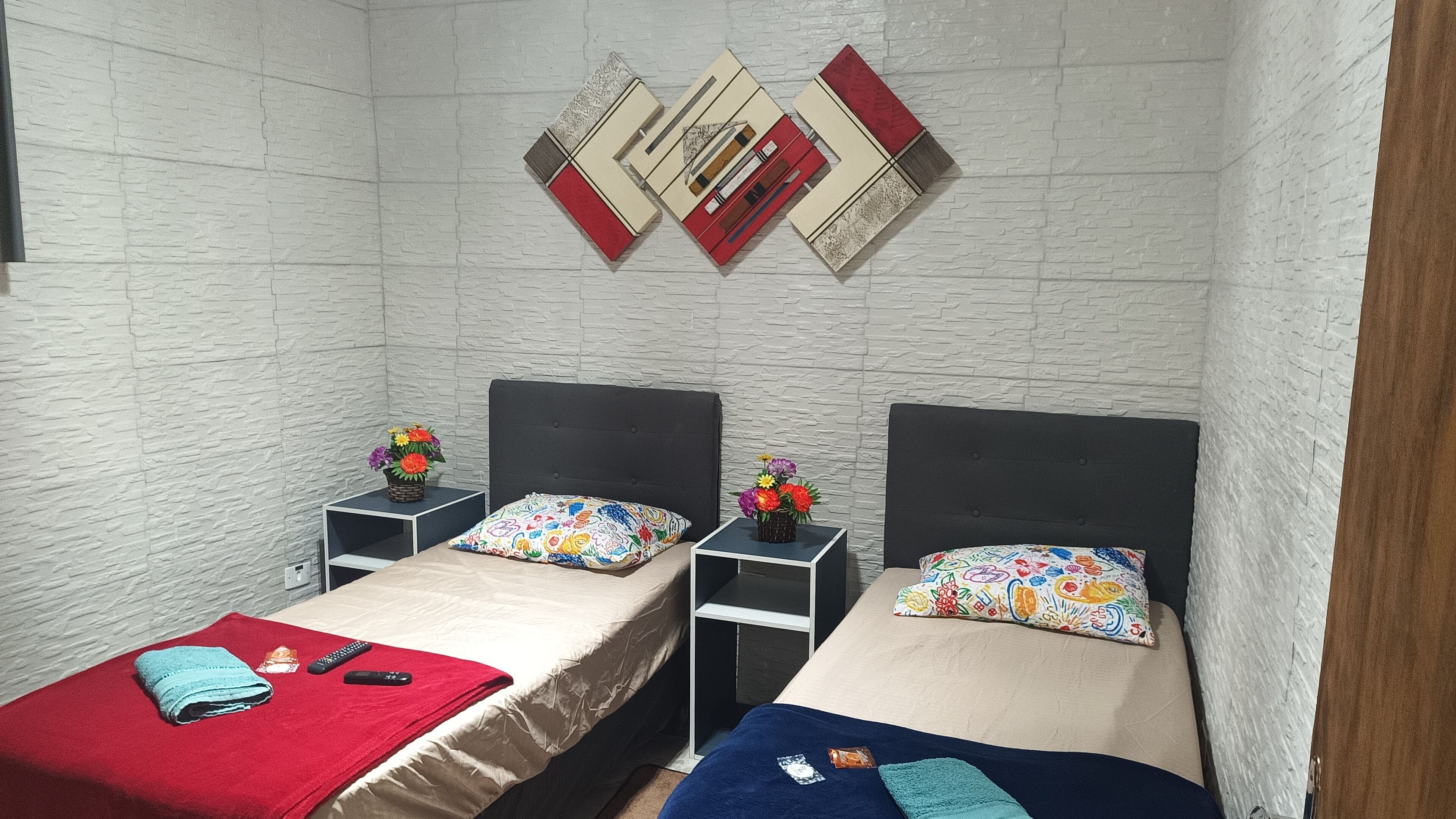 A room with two beds, each with a headboard and a nightstand. There are decorative pillows and a small vase with flowers on each nightstand.